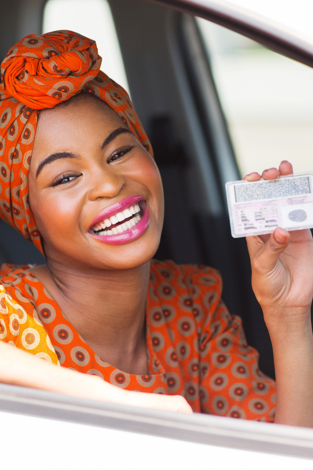 Jeune femme africaine souriante dans une voiture. elle tiens sa carte de permis de conduire qu'elle vient d'obtenir